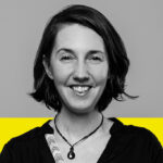 Marie-Blanche est en noir et blanc. Elle porte un haut noir avec un collier et a les cheveux mi-longs. Le tiers inférieur de l'arrière-plan est jaune.Marie-Blanche is in black and white. She is wearing a black top with a necklace and has mid-length hair. The bottom third of the background is yellow.