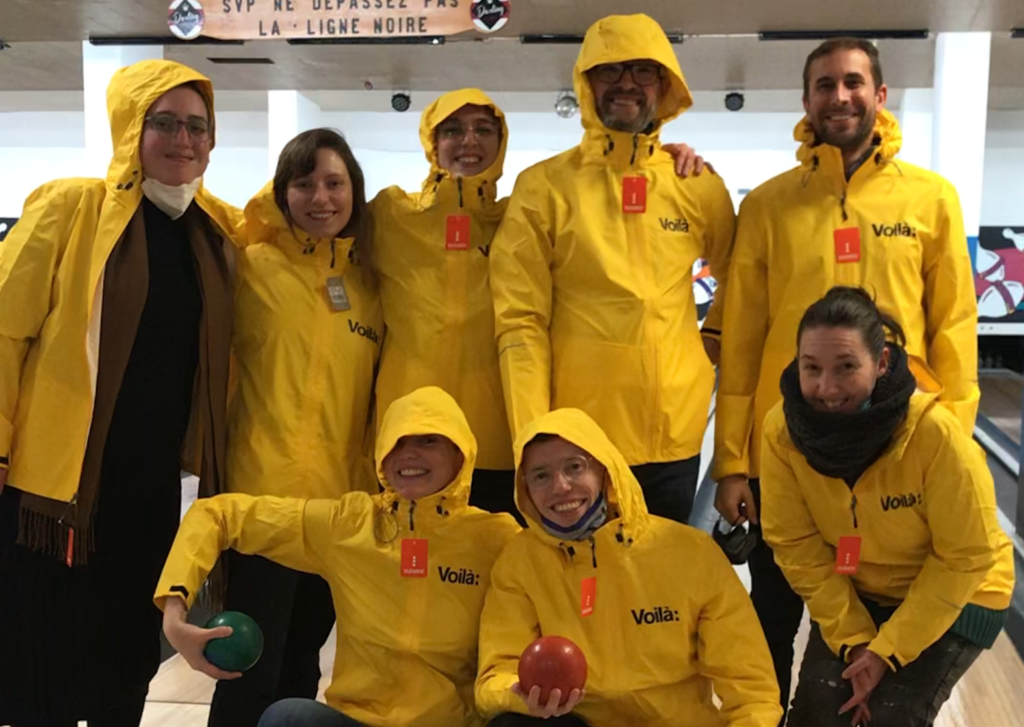 Photographie de l'équipe de Voilà: portant fièrement des imperméables jaunes dans une allée de quilles