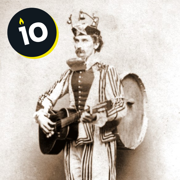 American one-man band from 1865. His guitar is in his arms, his harmonica in front of his face, his drum on his back and a triangle at his feet.