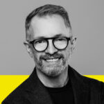 Francis Gagnon en noir et blanc, portant des lunettes et un veston. Le tiers inférieur de l'arrière-plan est jaune. Francis Gagnon in black and white, wearing glasses and a jacket. The bottom third of the background is yellow.
