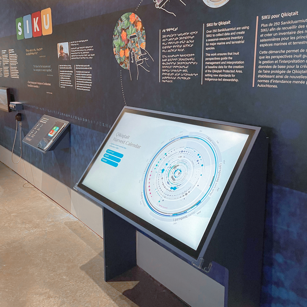 Photographie représentant l’expérience de la roue interactive des récoltes installée dans le Musée canadien de la nature. Positionné dans un angle de 45 degrés à la verticale pour faciliter l’interaction avec le public, un grand écran présente la vue de l’écran d'accueil de l’expérience. Il est placé à une hauteur d’environ trois pieds du sol afin de faciliter son utilisation.